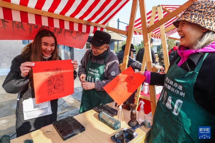 12月31日，外國留學(xué)生（左一）在年貨節(jié)現(xiàn)場體驗用雕版印刷技藝印制年畫。