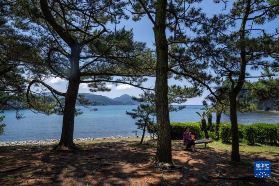 6月12日，在日本静冈县贺茂郡西伊豆町堂之岛公园，一名游客坐在海边。伊豆八景之一的堂之岛位于伊豆半岛西海岸的海湾内，有许多小岛星罗棋布地散落其间。新华社记者 张笑宇 摄