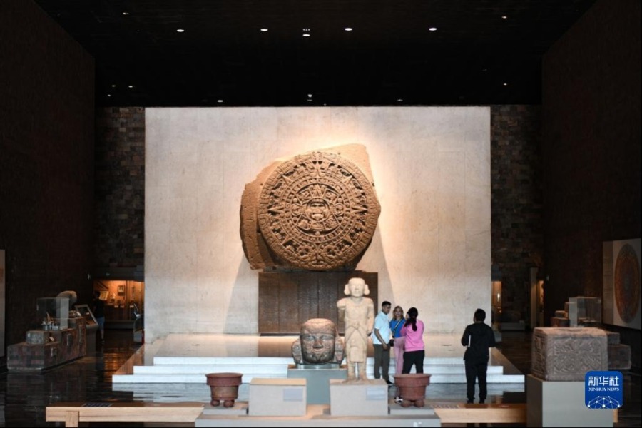 5月10日，游客在墨西哥首都墨西哥城的人类学博物馆参观时以太阳历石（后）为背景留影。新华社记者 辛悦卫 摄