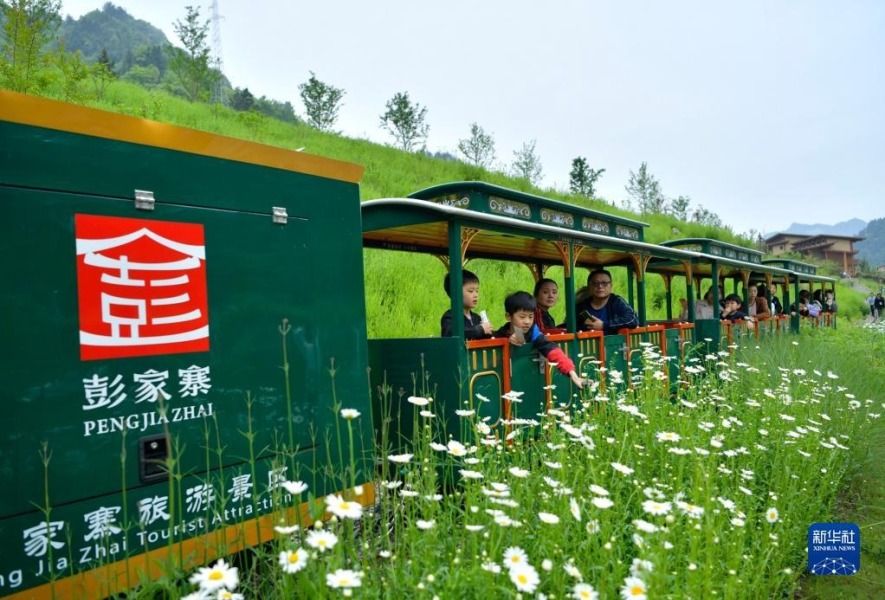 5月3日，游客在湖北省宣恩县彭家寨古吊脚楼前体验“小火车”。新华社发（宋文 摄）